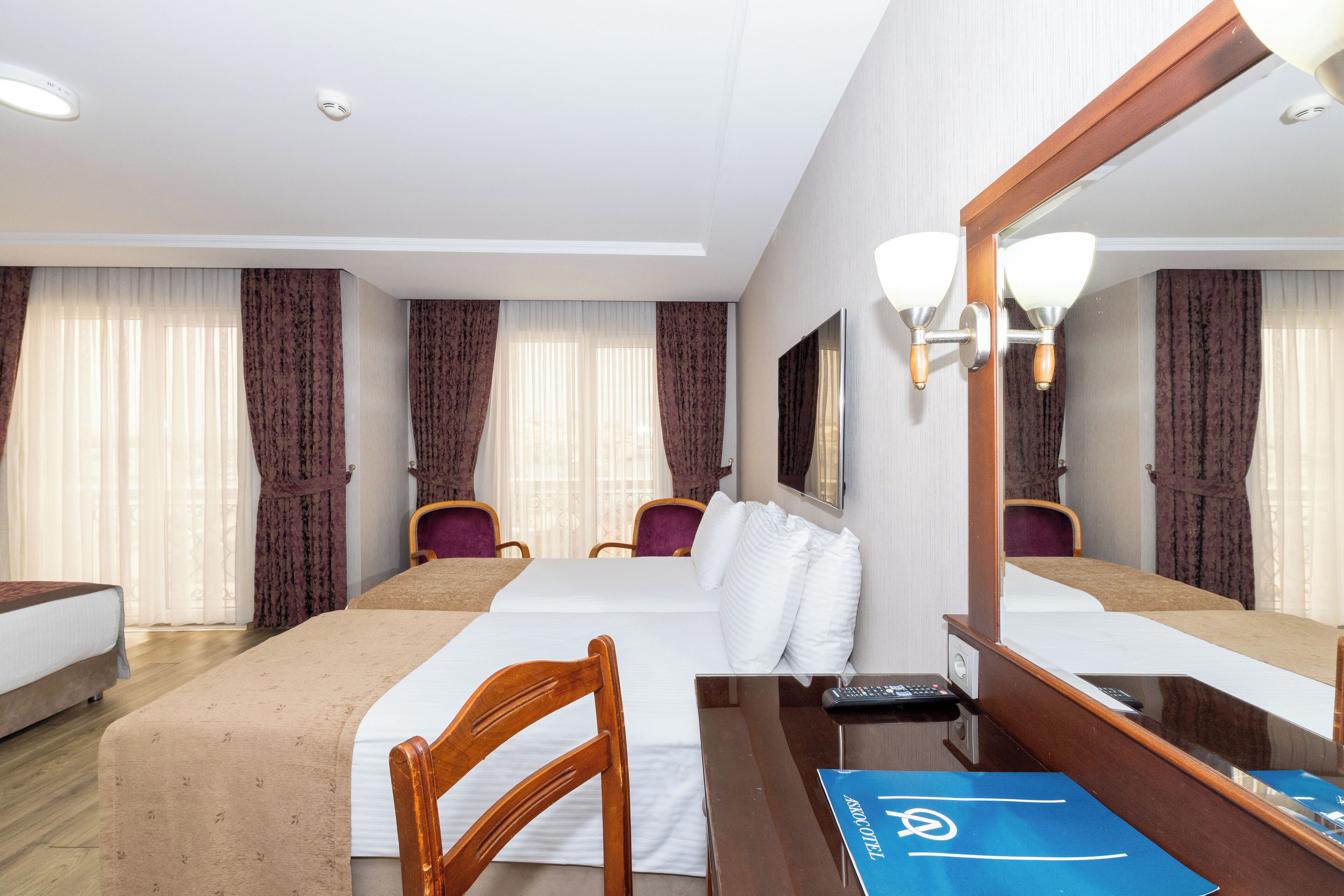 A hotel room with a large bed, a desk with a computer, a chair, and a mirror.