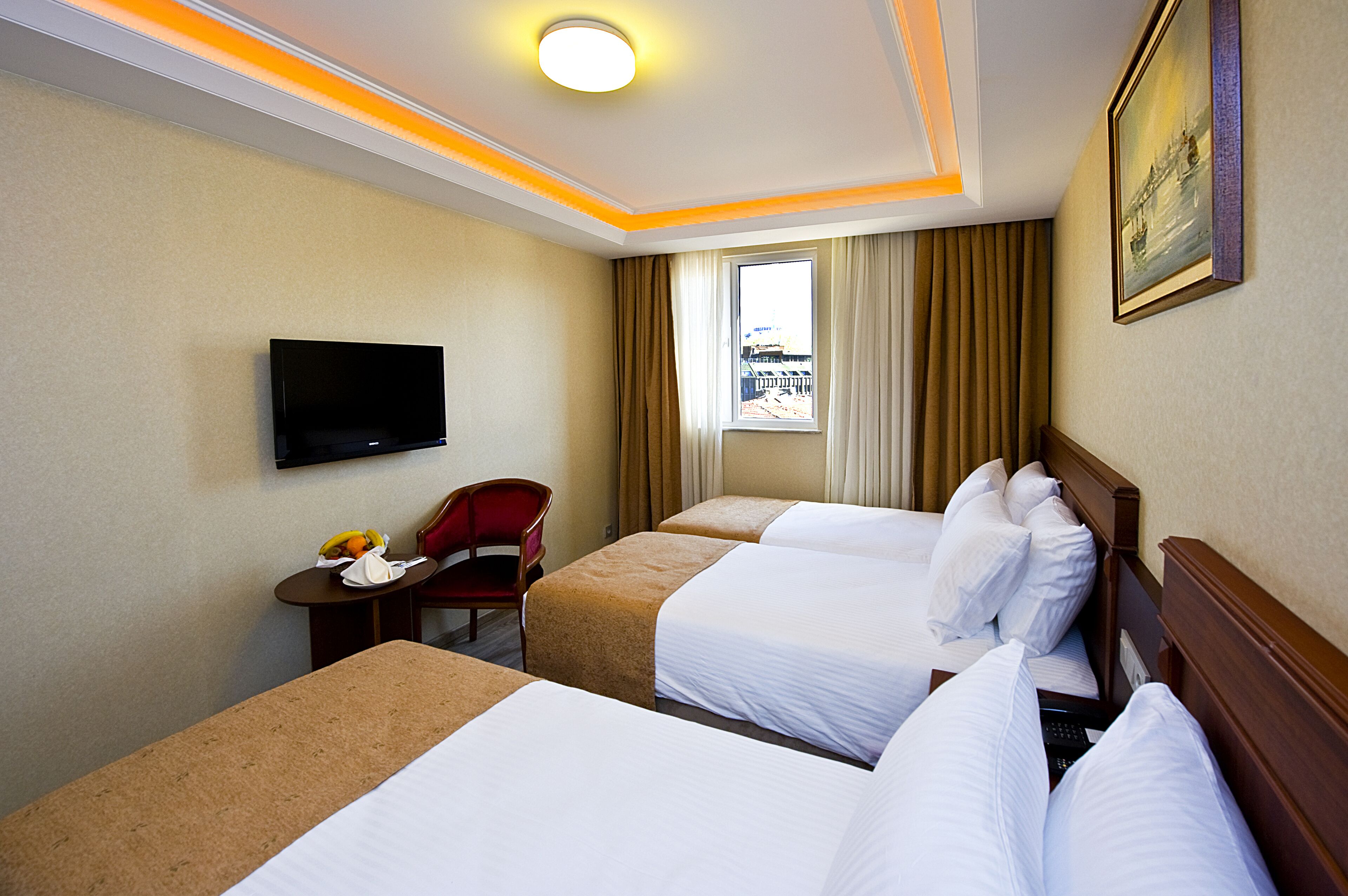 A hotel room with two beds, a TV, a small table with fruit, and a window with curtains.