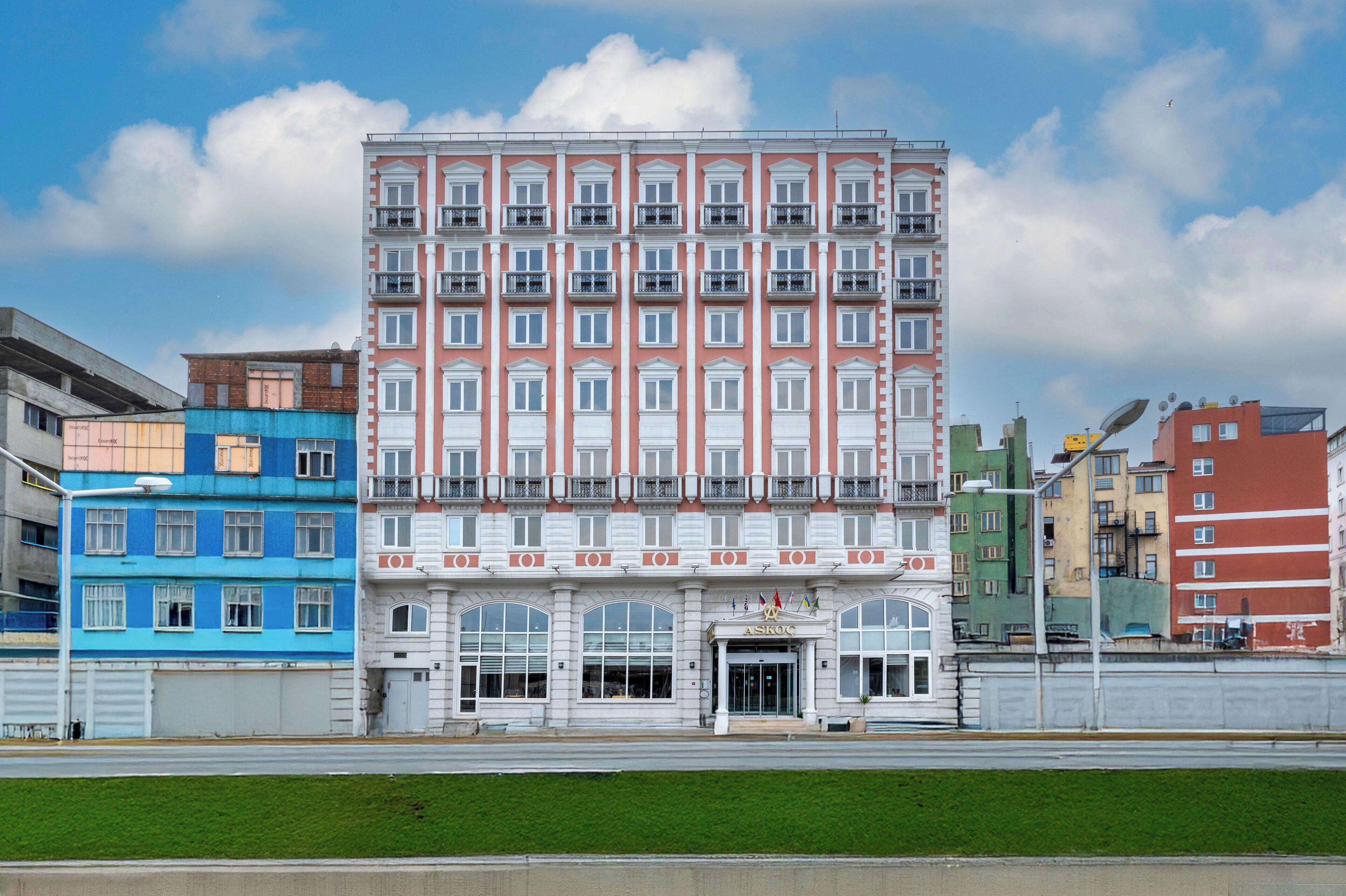 A multi-story hotel with a central entrance, balconies, and a clear sky.