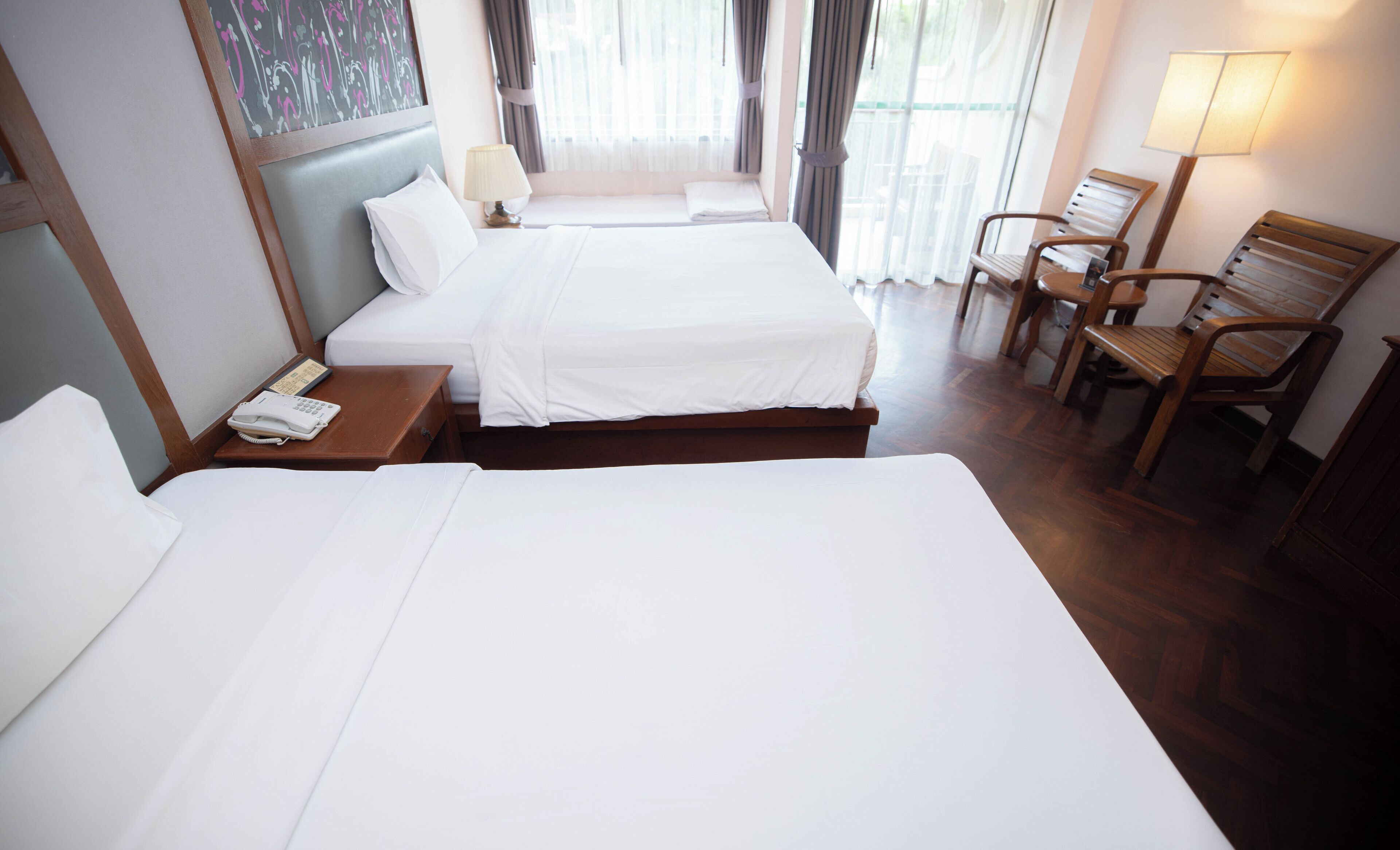 A hotel room with two beds, a bedside table with a phone, a lamp, and a chair.