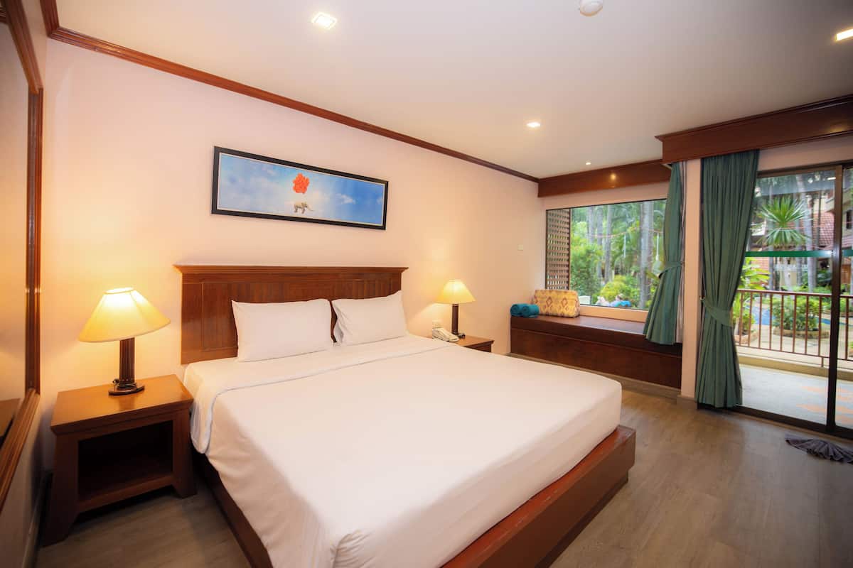 A hotel room with a large bed, two bedside tables with lamps, a nightstand, a window with curtains, and a framed picture on the wall.