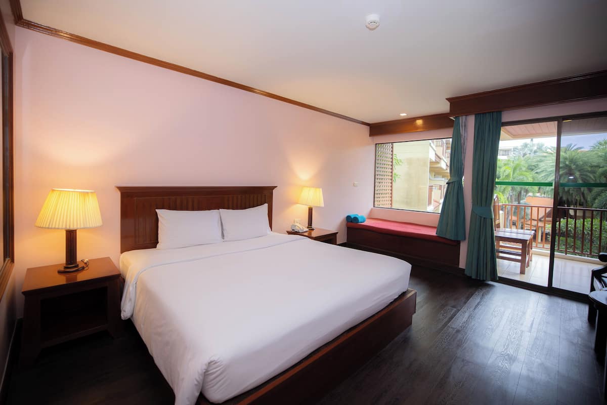 A hotel room with a large bed, two bedside lamps, a nightstand, and a view of a balcony with outdoor seating.