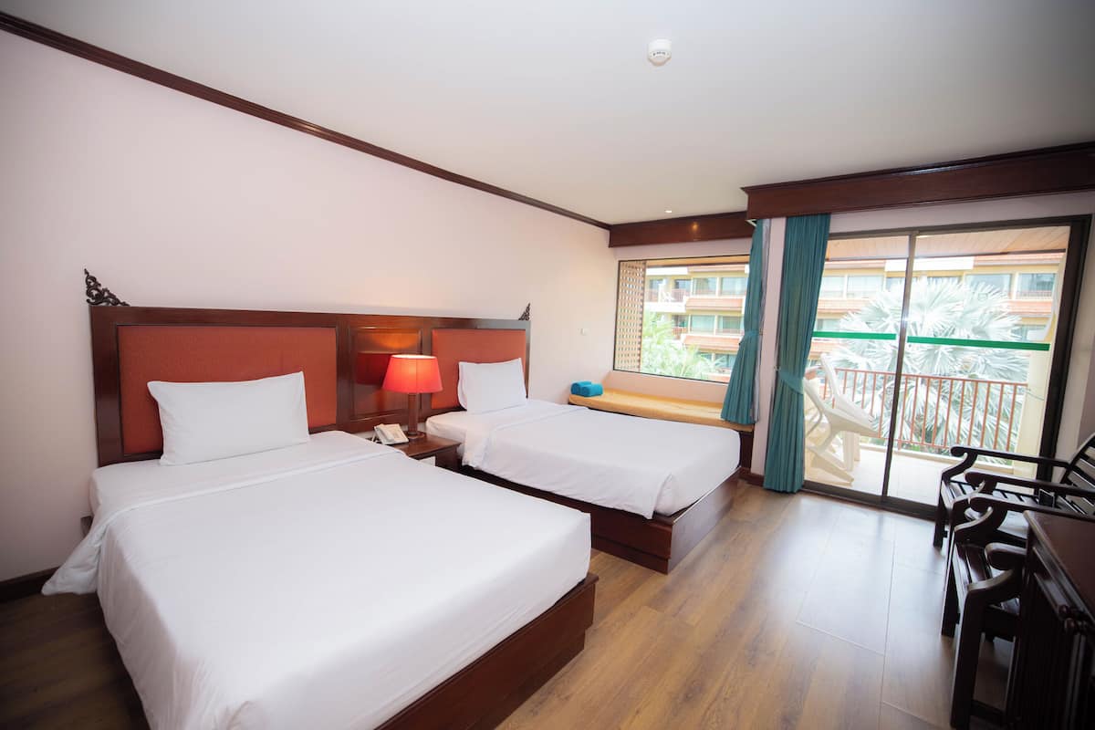 A hotel room with two beds, a desk, and a balcony with a view of palm trees.