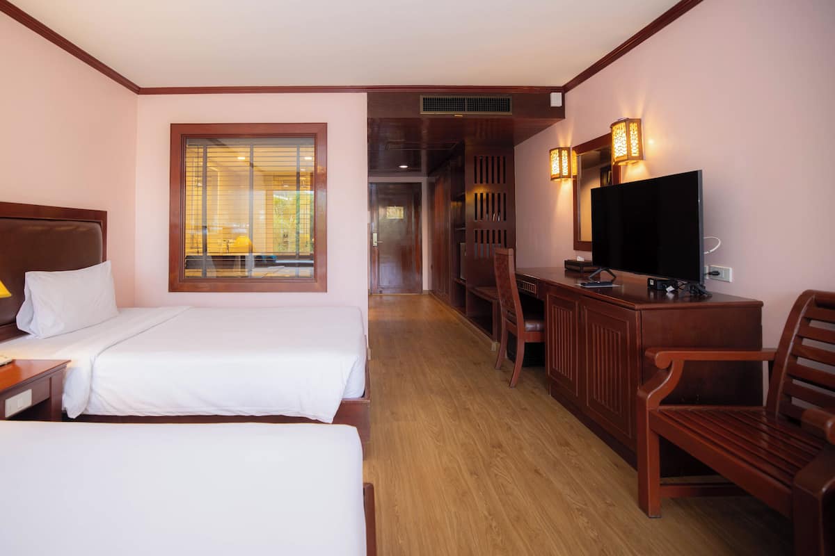 A hotel room with two beds, a desk with a TV, a chair, a lamp, and a window with blinds.