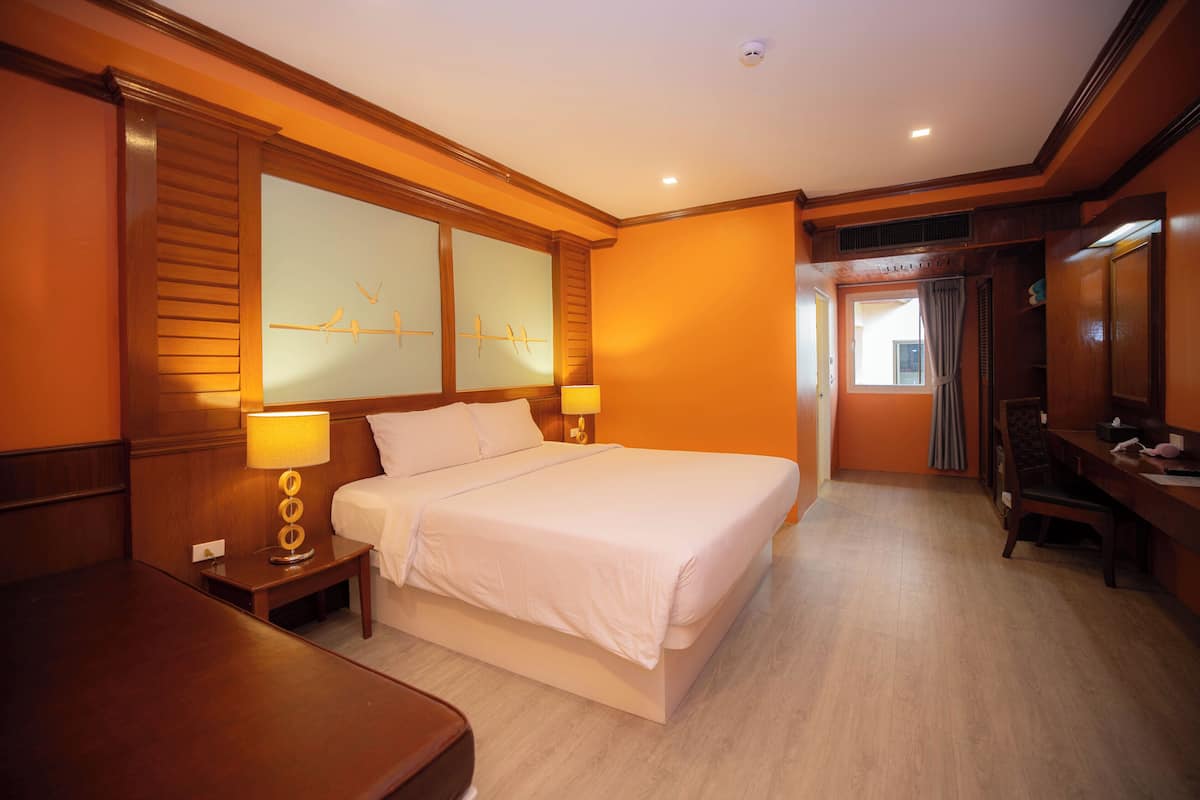 A hotel room with a large bed, two bedside tables with lamps, a wooden headboard, and a large window with curtains.