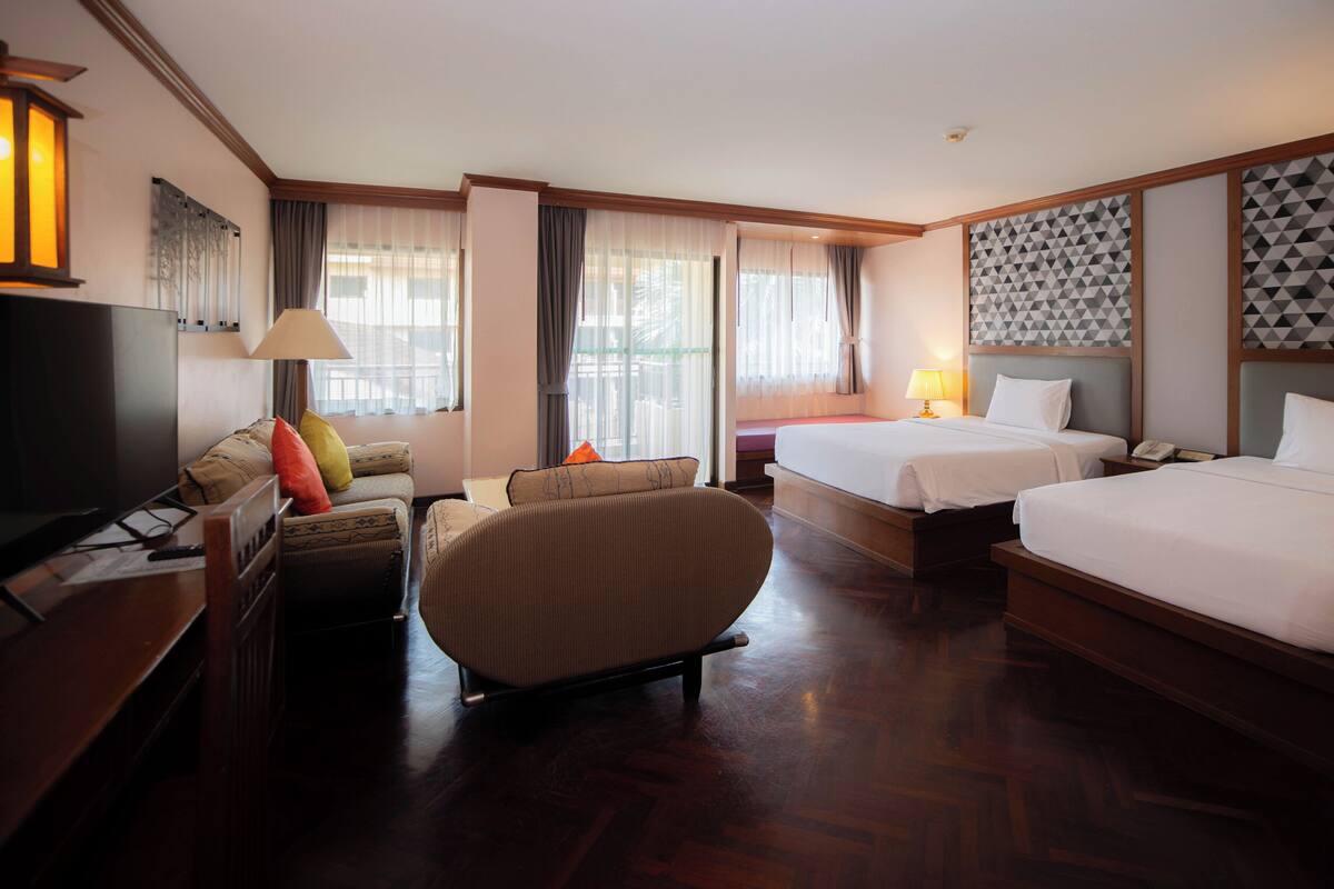 A hotel room with two beds, a sofa, a TV, and a desk.