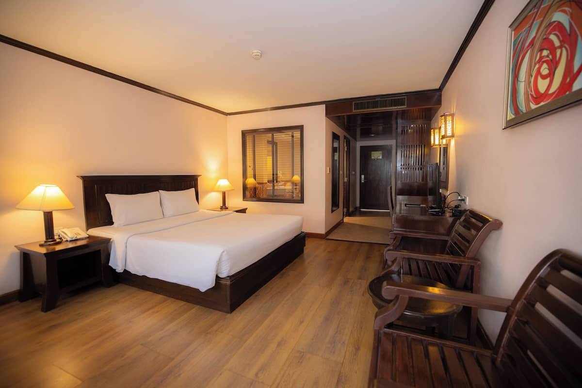 A hotel room with a bed, bedside lamps, a desk with a phone, a dining area with chairs and a table, and a door leading to a hallway.