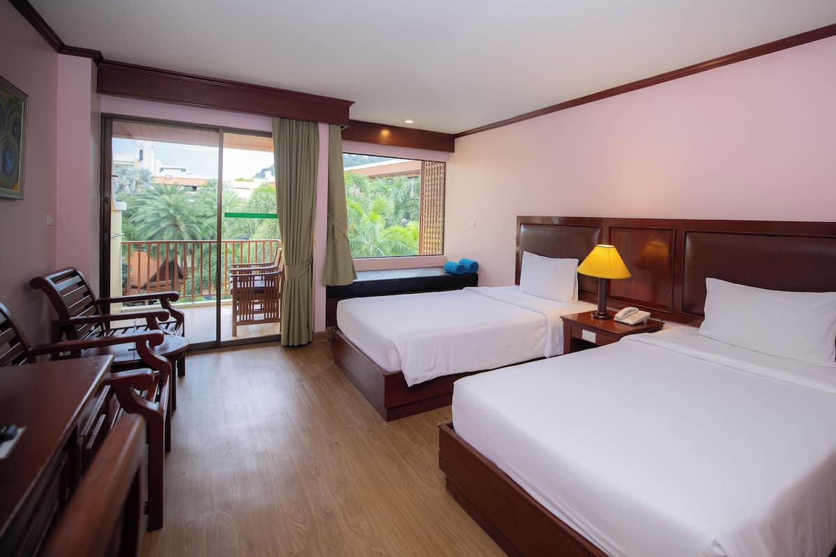 A hotel room with two beds, a balcony with a table and chairs, and a wooden desk.
