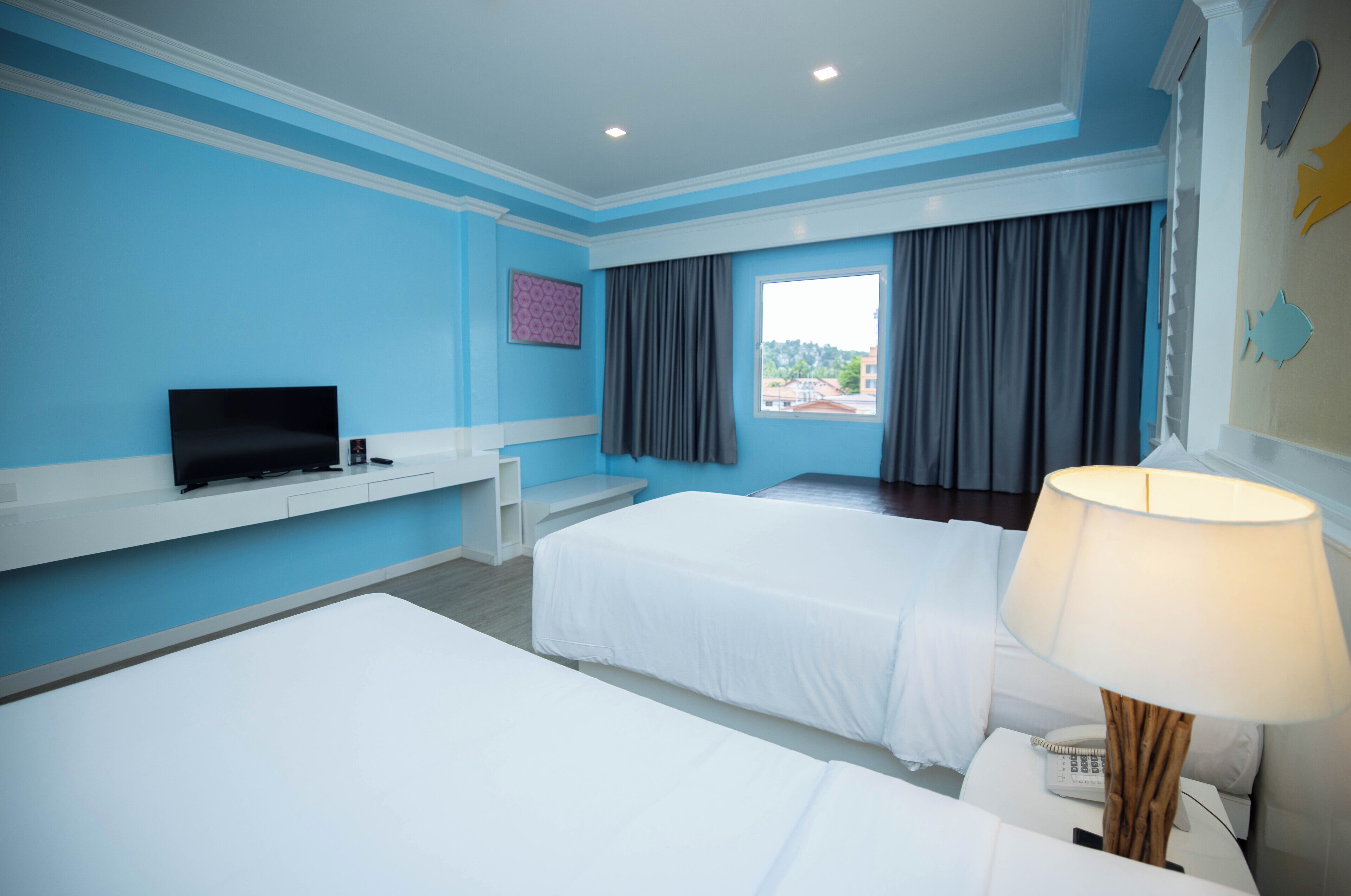 A hotel room with two beds, a TV, a desk, and a window with curtains.