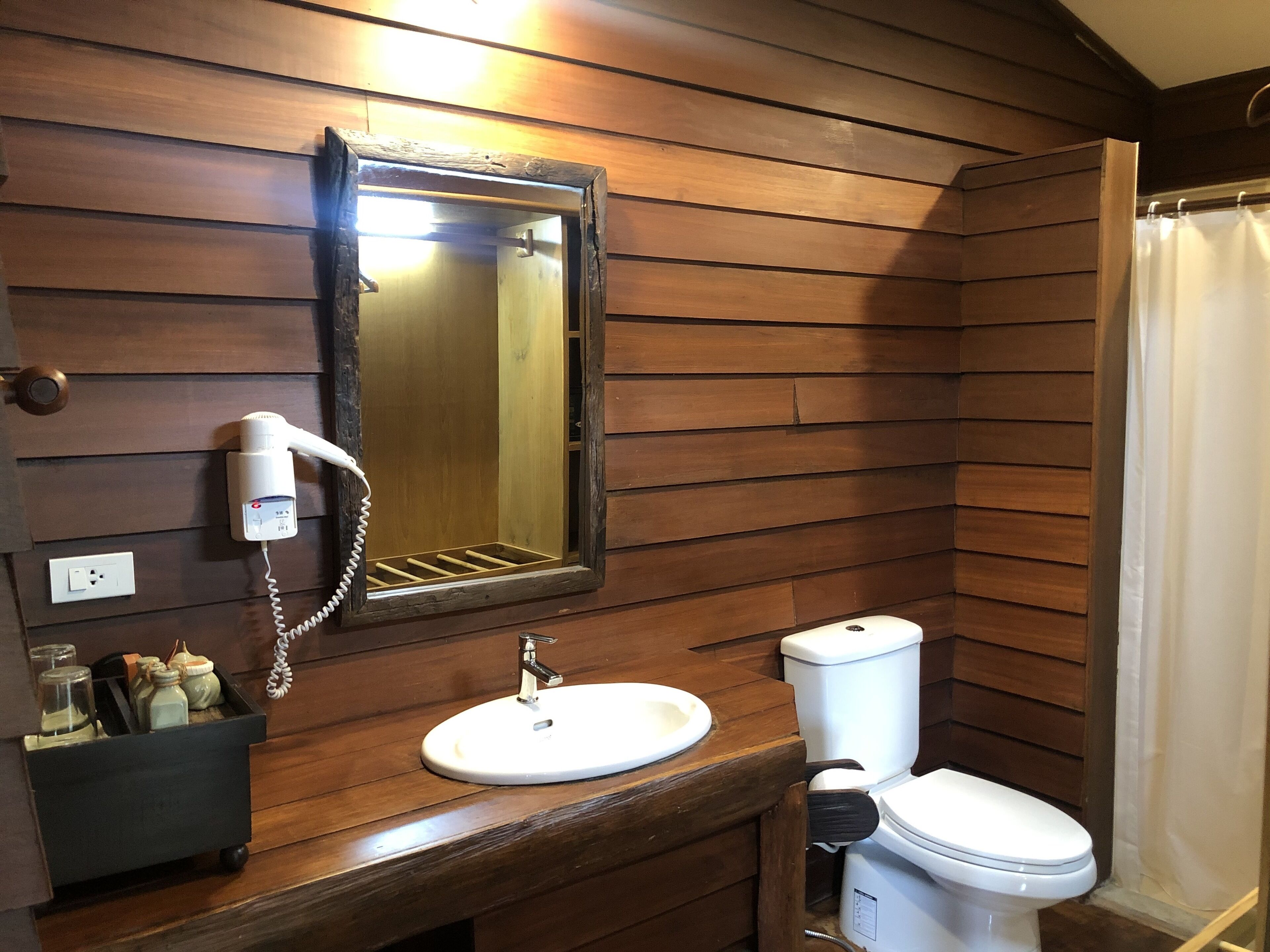 Un baño con paneles de madera, un lavabo, un inodoro y un secador de pelo fijado a la pared.