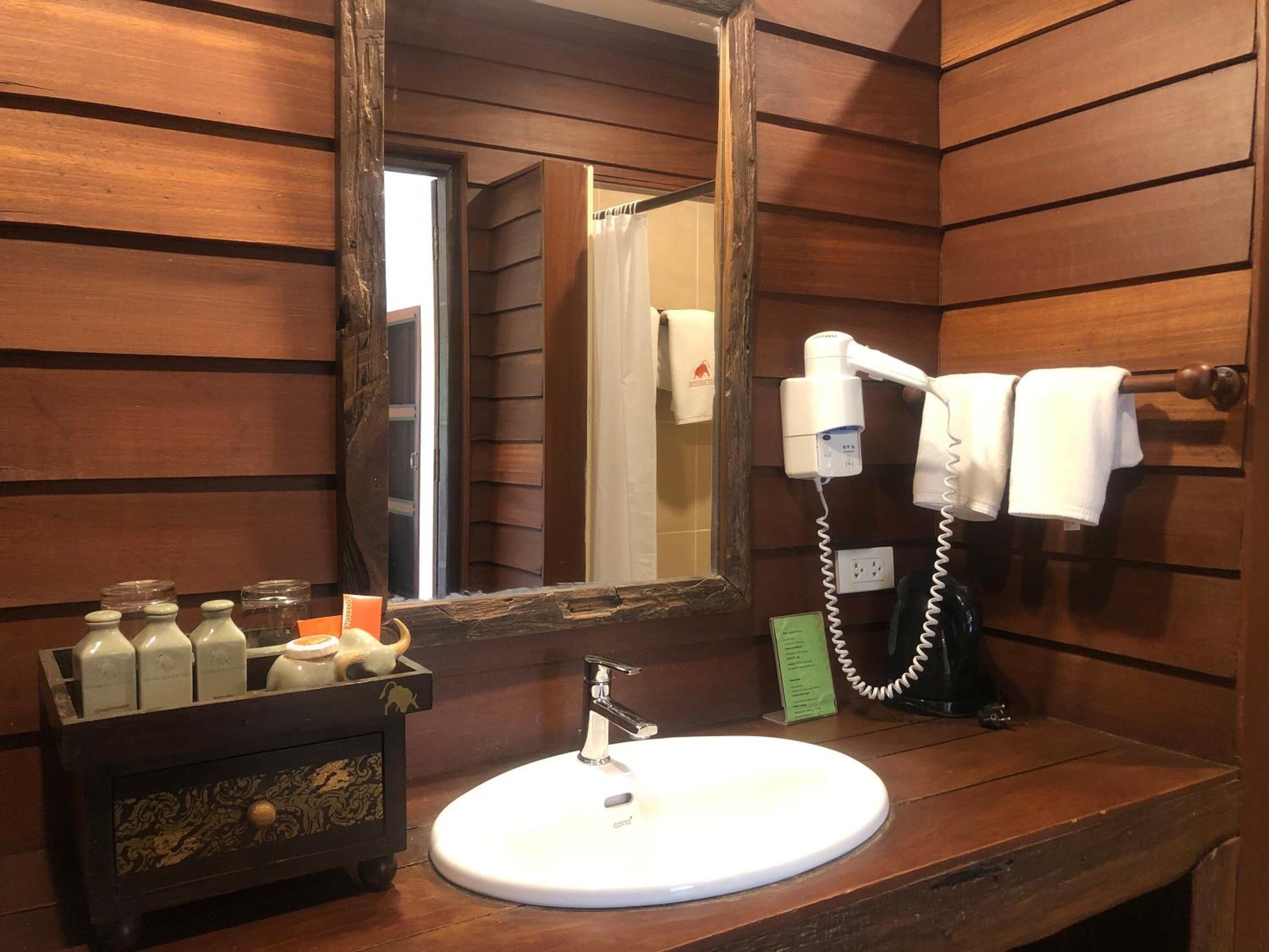 A wooden cabin-style bathroom with a large mirror, a white sink, and a hairdryer.