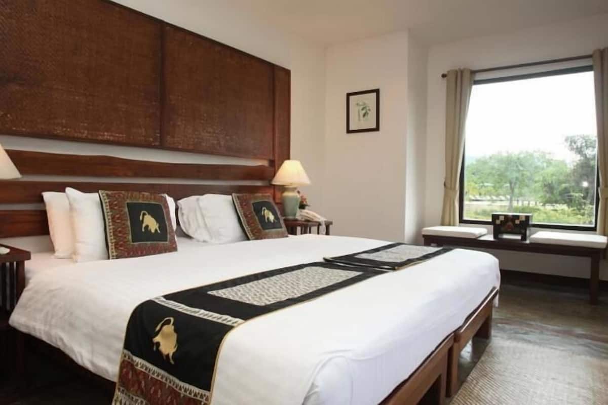 Quarto de hotel com uma cama grande, duas mesas de cabeceira com luminárias, uma janela com vista e um quadro na parede.