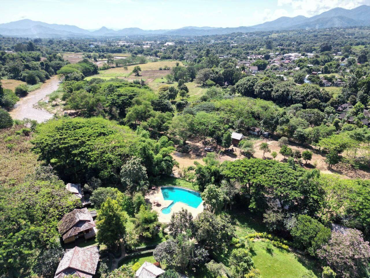 Ein großer, rechteckiger Swimmingpool, umgeben von üppiger Bepflanzung und Bäumen, mit Blick auf entfernte Berge und einen Fluss.