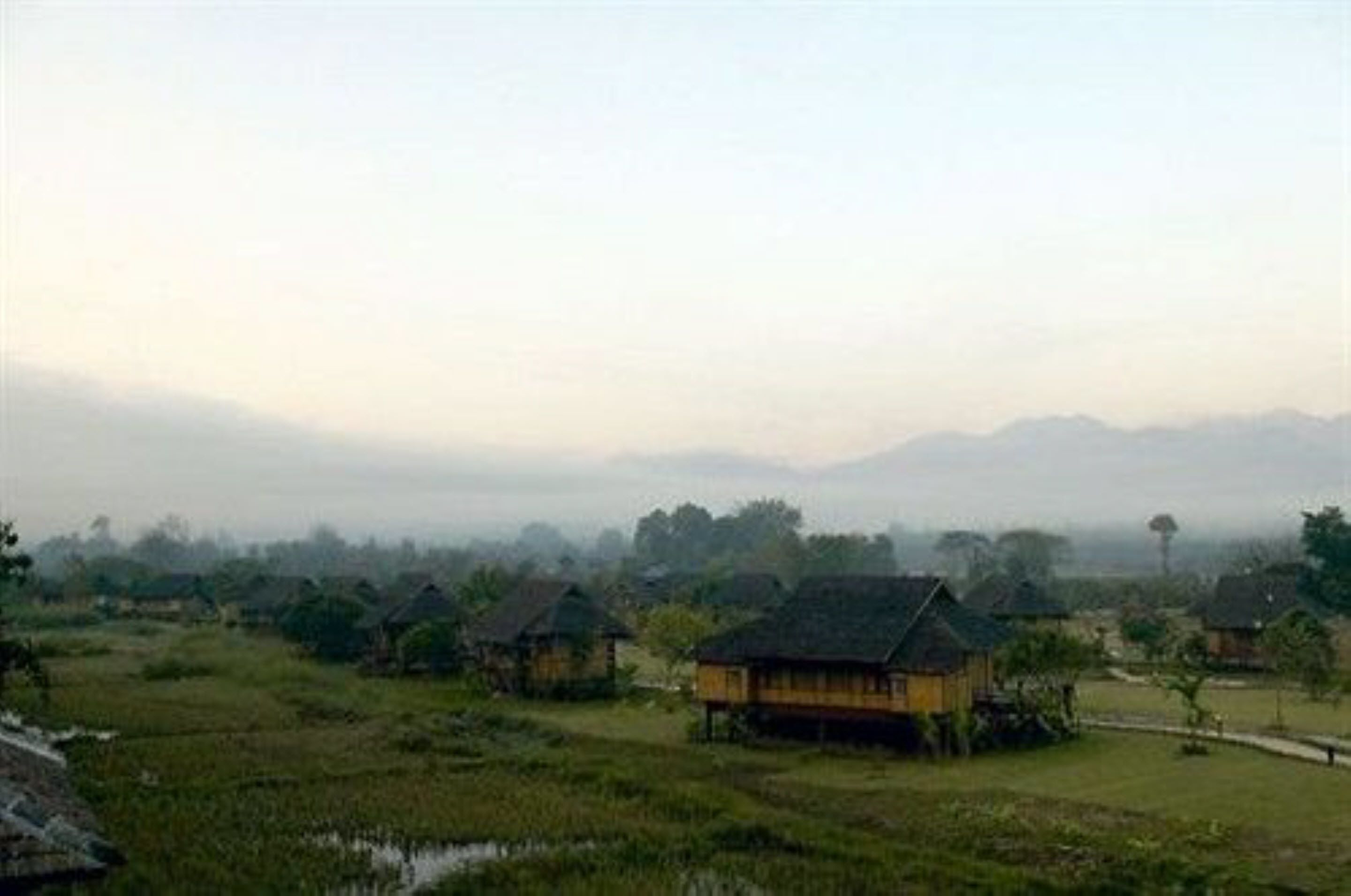 Un pueblo rural con casas tradicionales rodeado de campos y montañas al fondo.