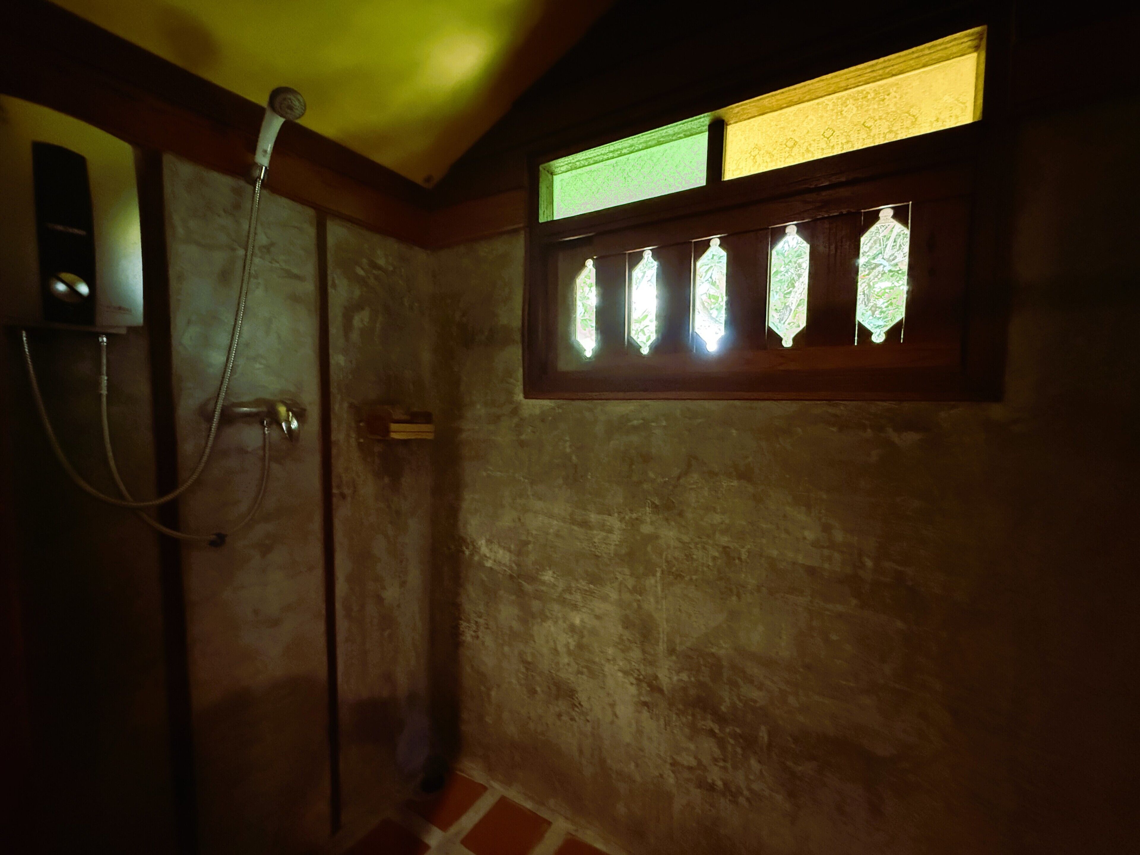 Un baño con ducha, una ventana con vidriera y un perchero.