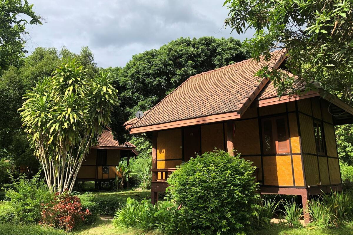 Um edifício em estilo tradicional com telhado de azulejos, rodeado por vegetação exuberante e árvores.