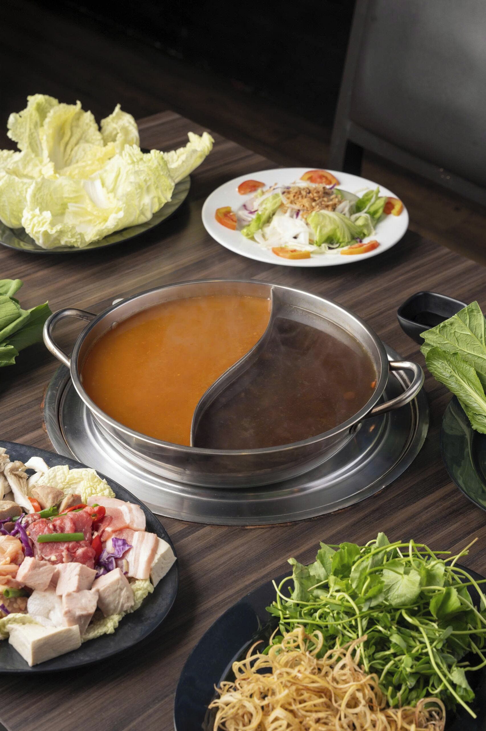 A table with a pot of soup, plates of food, and fresh vegetables.