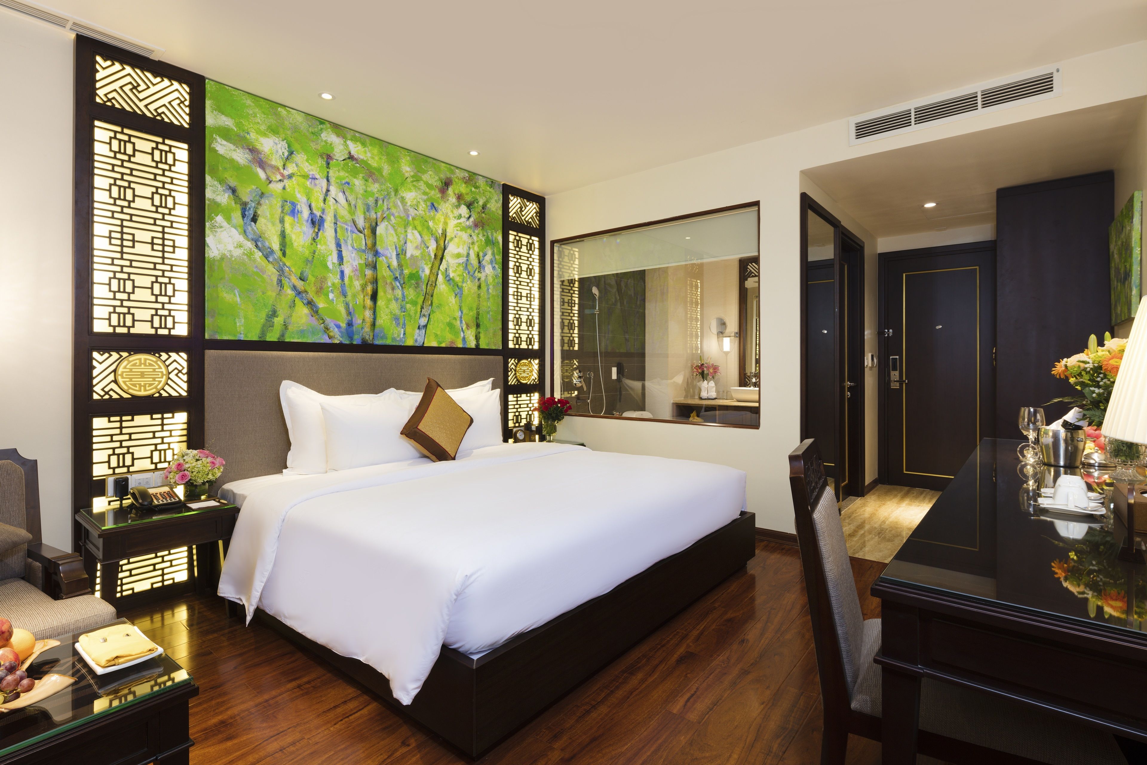 Een moderne hotelkamer met een groot bed, een bureau met spiegel en een decoratief wandpaneel.