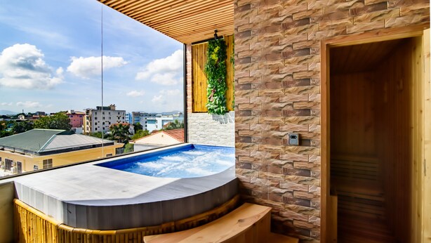 A modern spa area with a hot tub, wooden benches, and a stone wall. - Thanh Lich Royal Boutique Hotel (Hue)