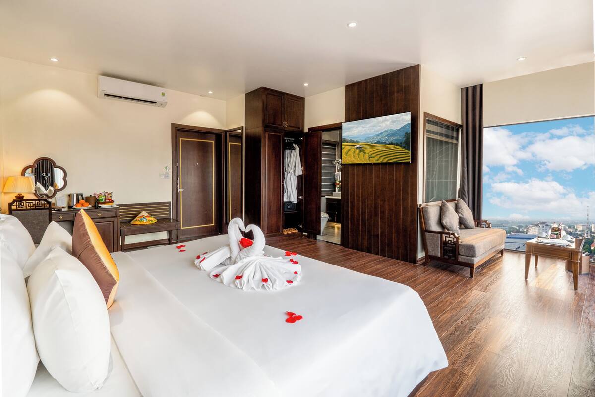 A hotel room with a large bed, a seating area with a view, and a wardrobe.
