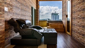 A modern room with a brick wall, a wooden ceiling, a sofa, an ottoman, and a view of a cityscape. - Thanh Lich Royal Boutique Hotel (Hue)