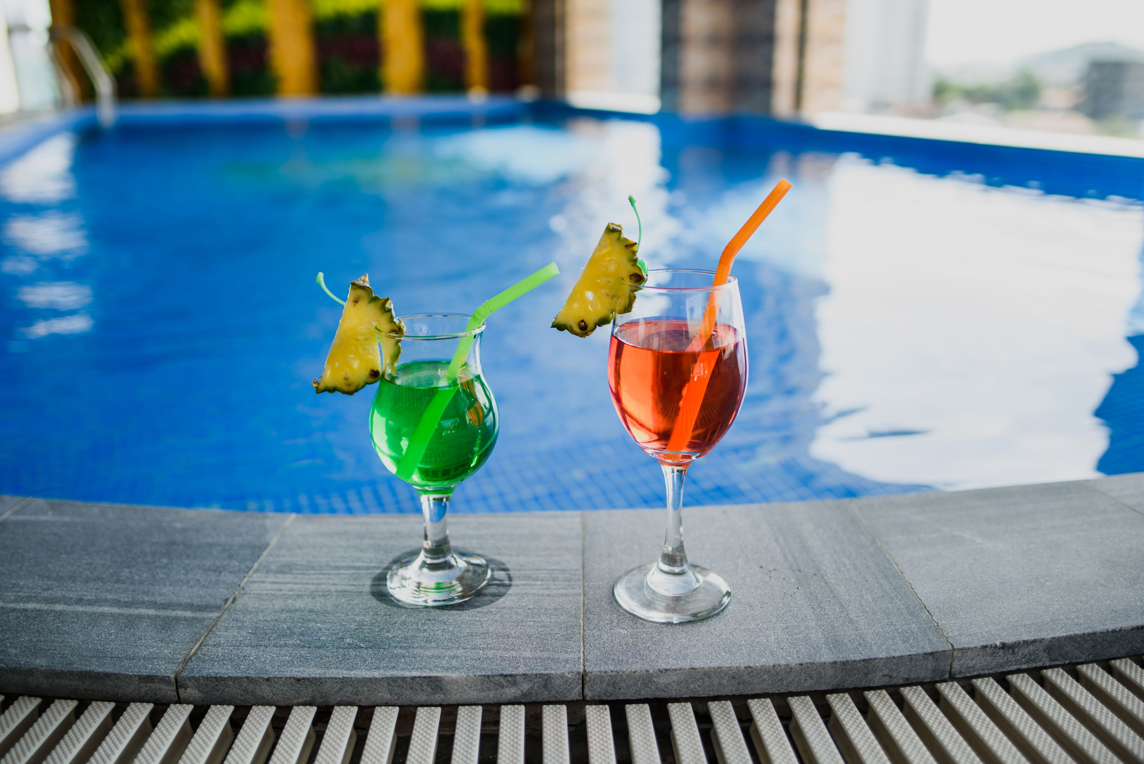 Two cocktails with garnishes on a poolside table.