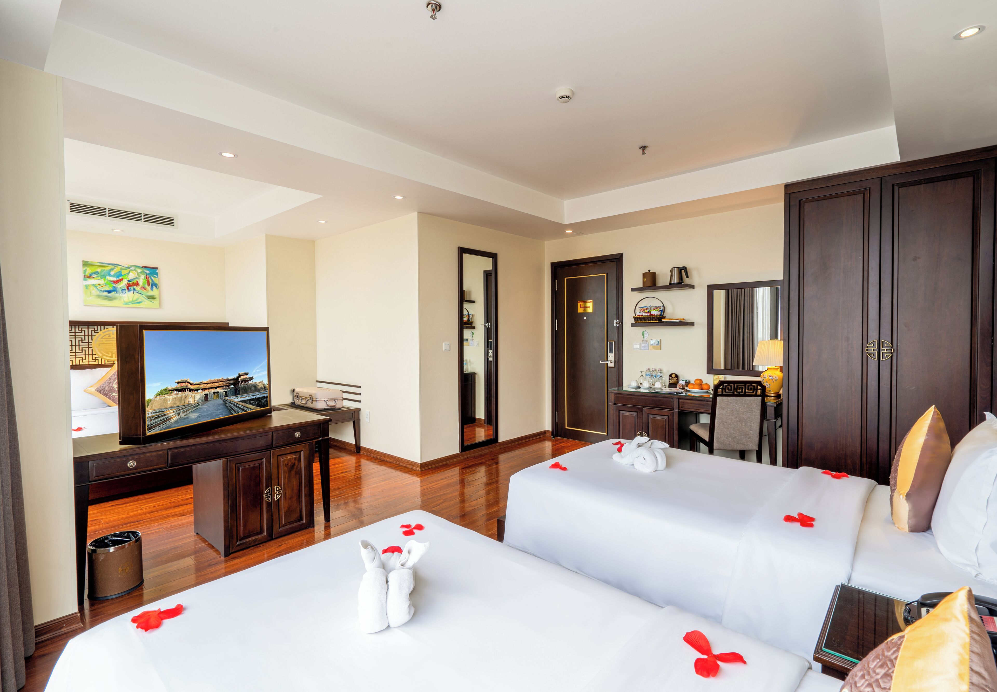 A hotel room with two beds, a desk, a television, and a bathroom.