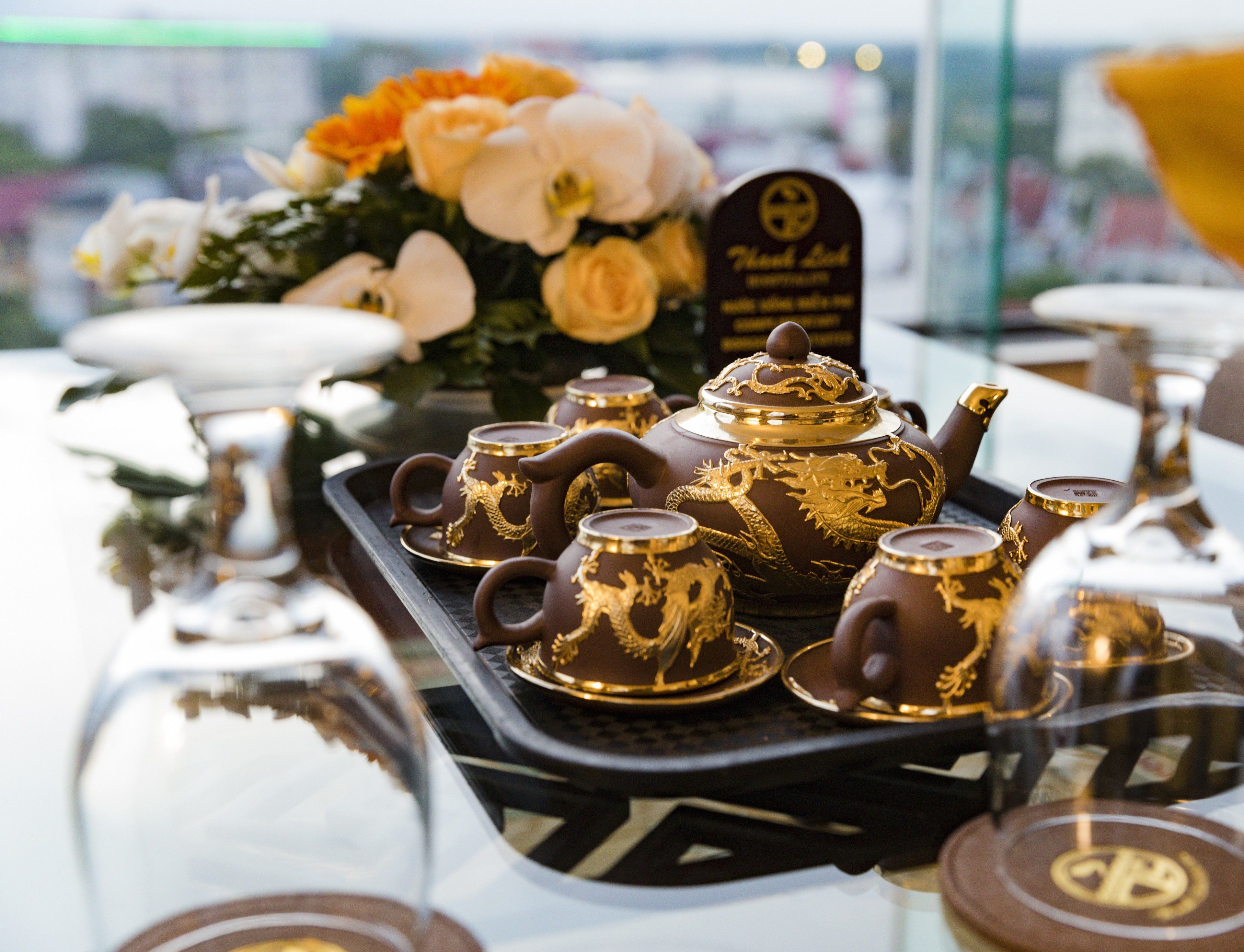 A tray with teapots and cups, a sign with a logo, and a bouquet of flowers.