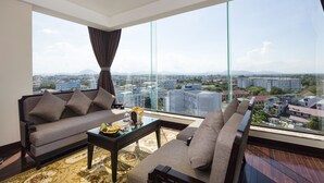A modern living room with a sofa, armchair, and coffee table, featuring a large window with a city view. - Thanh Lich Royal Boutique Hotel (Hue)