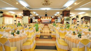 A banquet hall with round tables, yellow chairs, and a stage at the front. - Duy Tan Hotel (Hue)