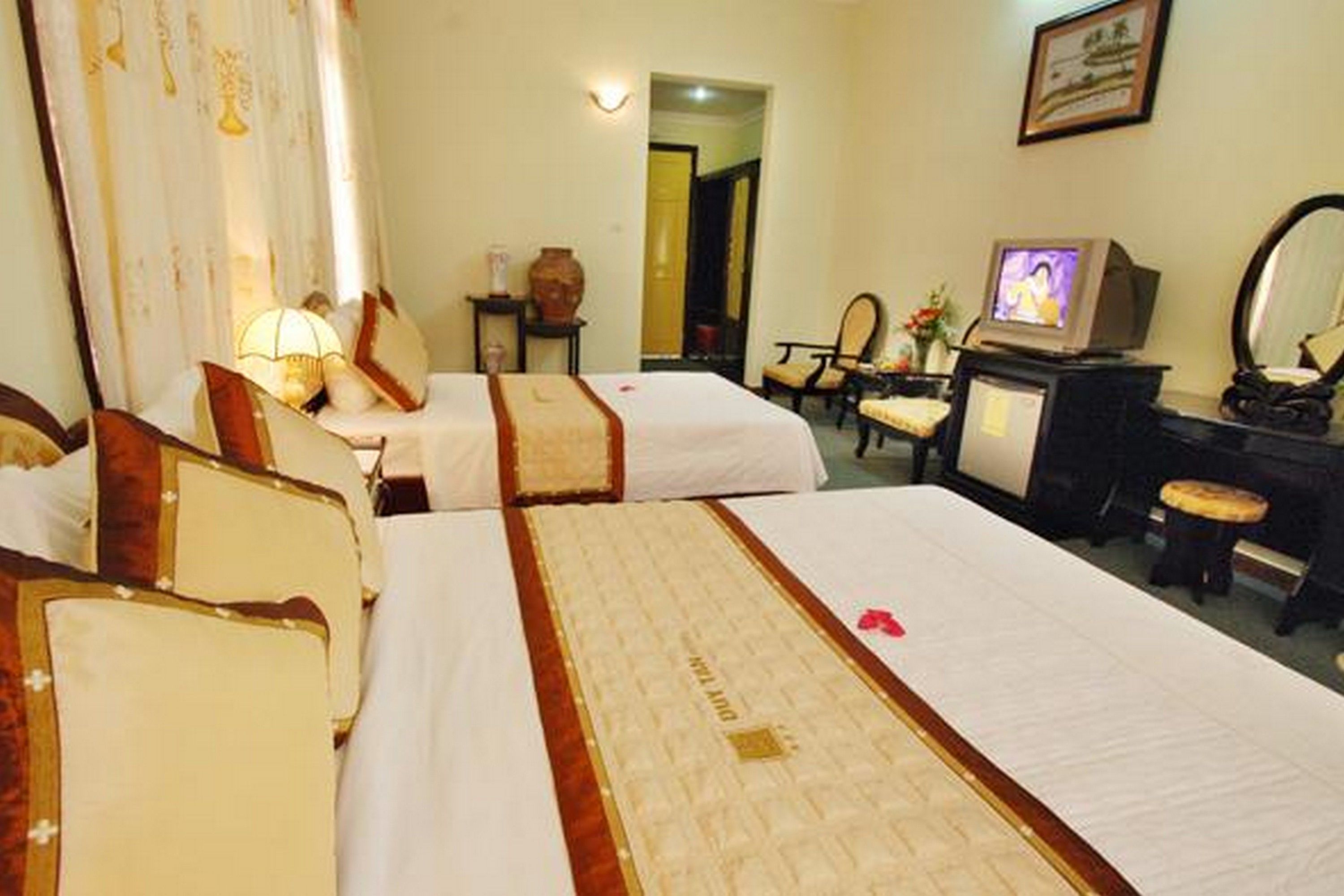 A hotel room with two beds, a television, a desk with a mirror, and a chair.