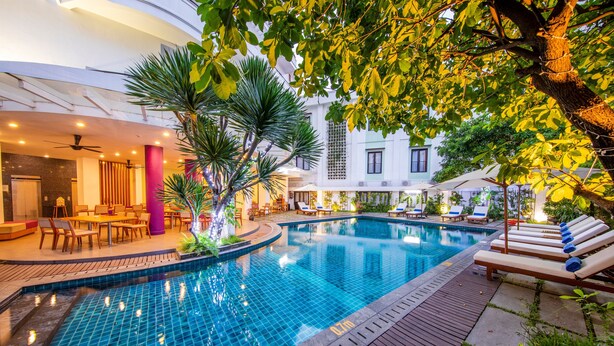 A swimming pool with lounge chairs and a dining area with tables and chairs. - ÊMM Hotel Hue (Hue)