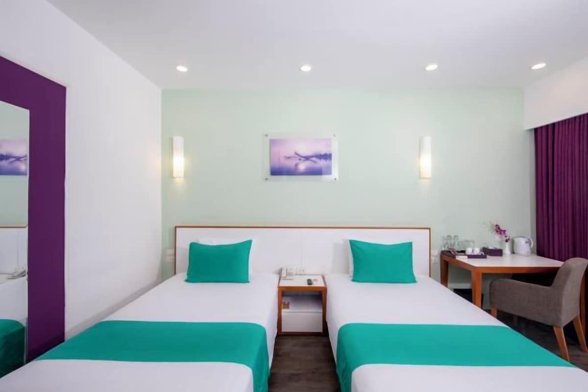 A hotel room with two single beds, a small desk with a chair, a nightstand, and a wall-mounted picture.