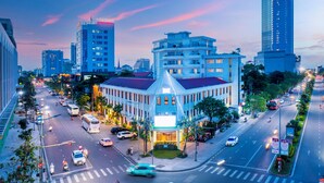 A modern hotel with a distinctive triangular roof, surrounded by a busy urban street at dusk. - ÊMM Hotel Hue (Hue)