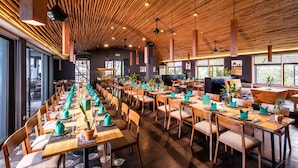 A spacious dining area with long wooden tables and chairs, large windows, and a high wooden ceiling. - ÊMM Hotel Hue (Hue)