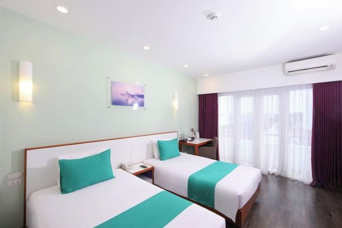 A hotel room with two beds, a nightstand, a desk, and an air conditioning unit.