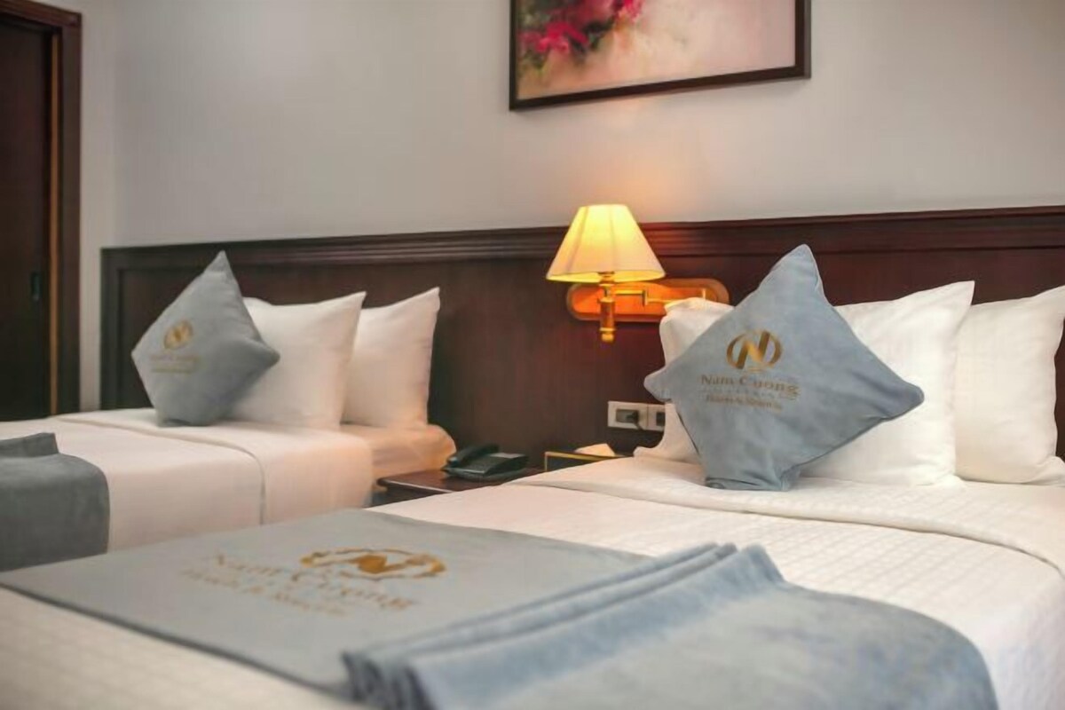 A hotel room with two beds, a nightstand, a lamp, and a painting on the wall.