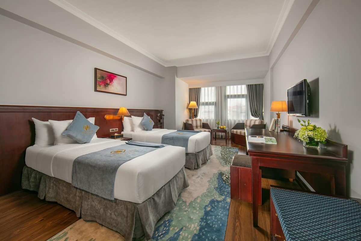 A hotel room with two beds, a desk, a TV, and a window with curtains.