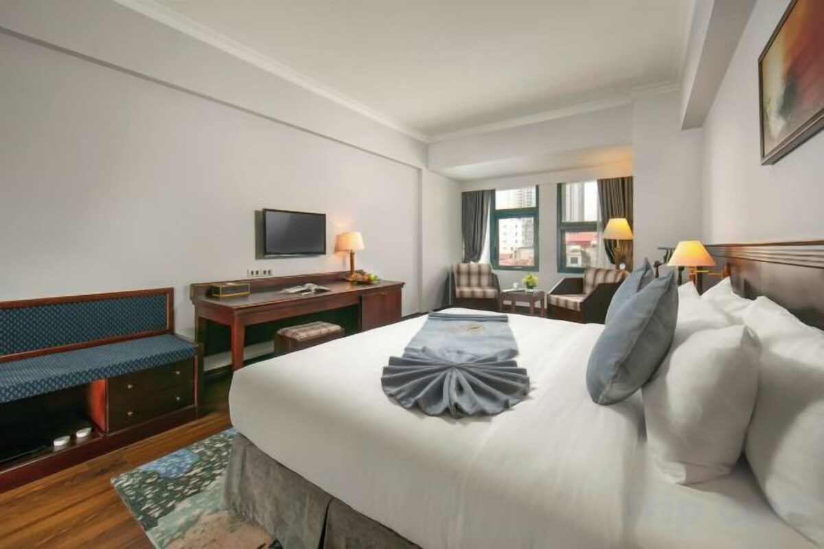 A hotel room with a bed, a desk, a television, and a window with curtains.