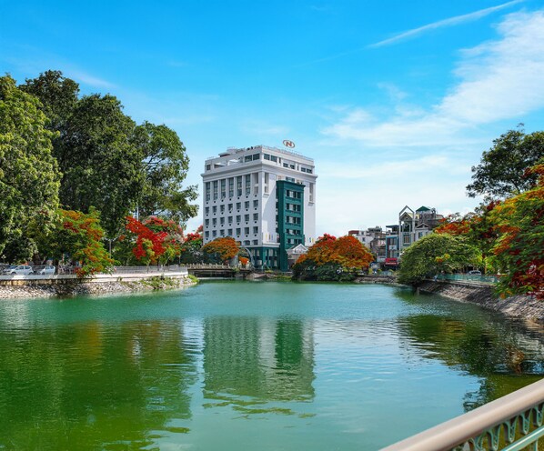 A hotel with a large building, a body of water, and surrounding trees. - The Tray Hotel Hai Phong (Hai Phong)