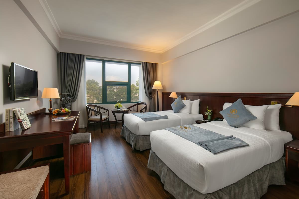 A hotel room with two beds, a desk, a TV, and a window with curtains.