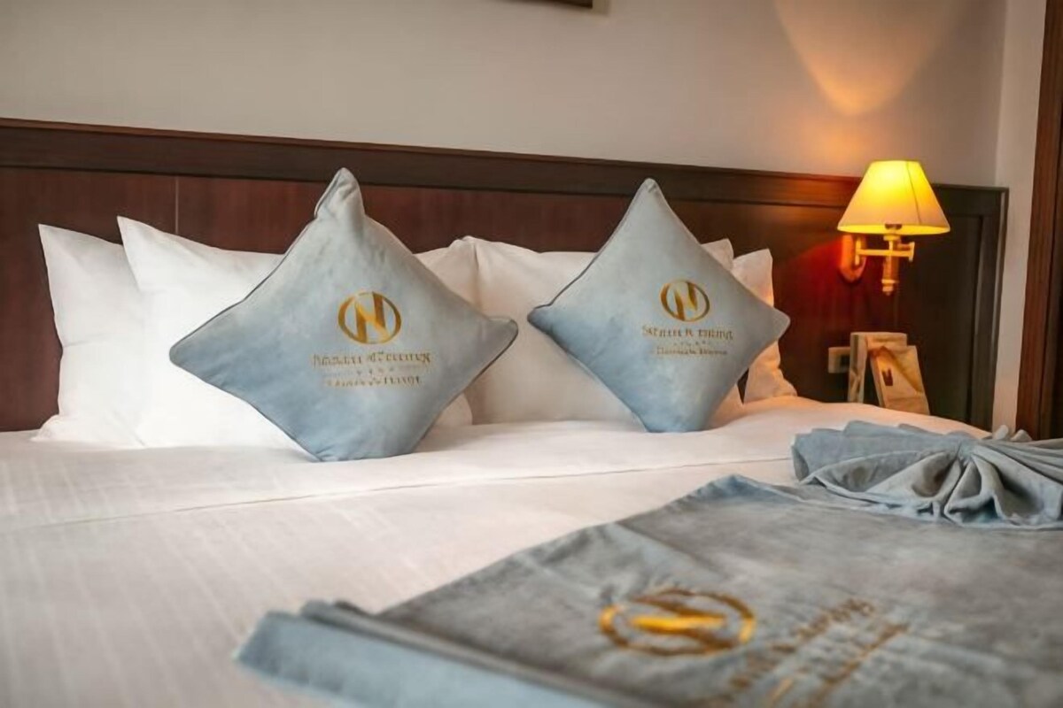 A neatly made bed with two pillows, a bedside lamp, and a folded towel.