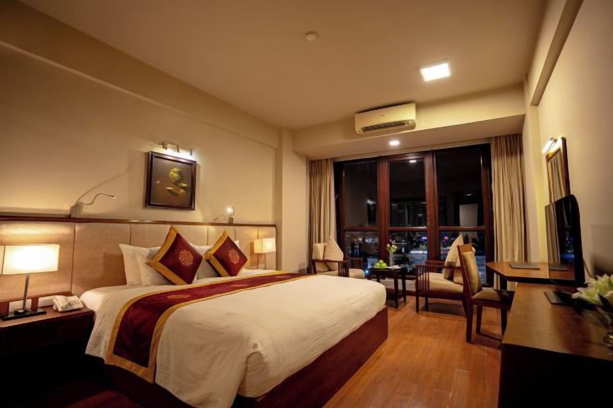 A hotel room with a large bed, bedside tables, a desk, and a chair.