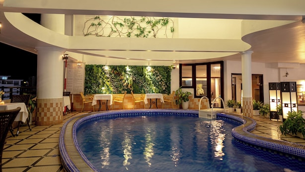 A swimming pool with a tiled edge, surrounded by tables and chairs, and a wall with greenery. - Asia Hotel Hue (Hue)