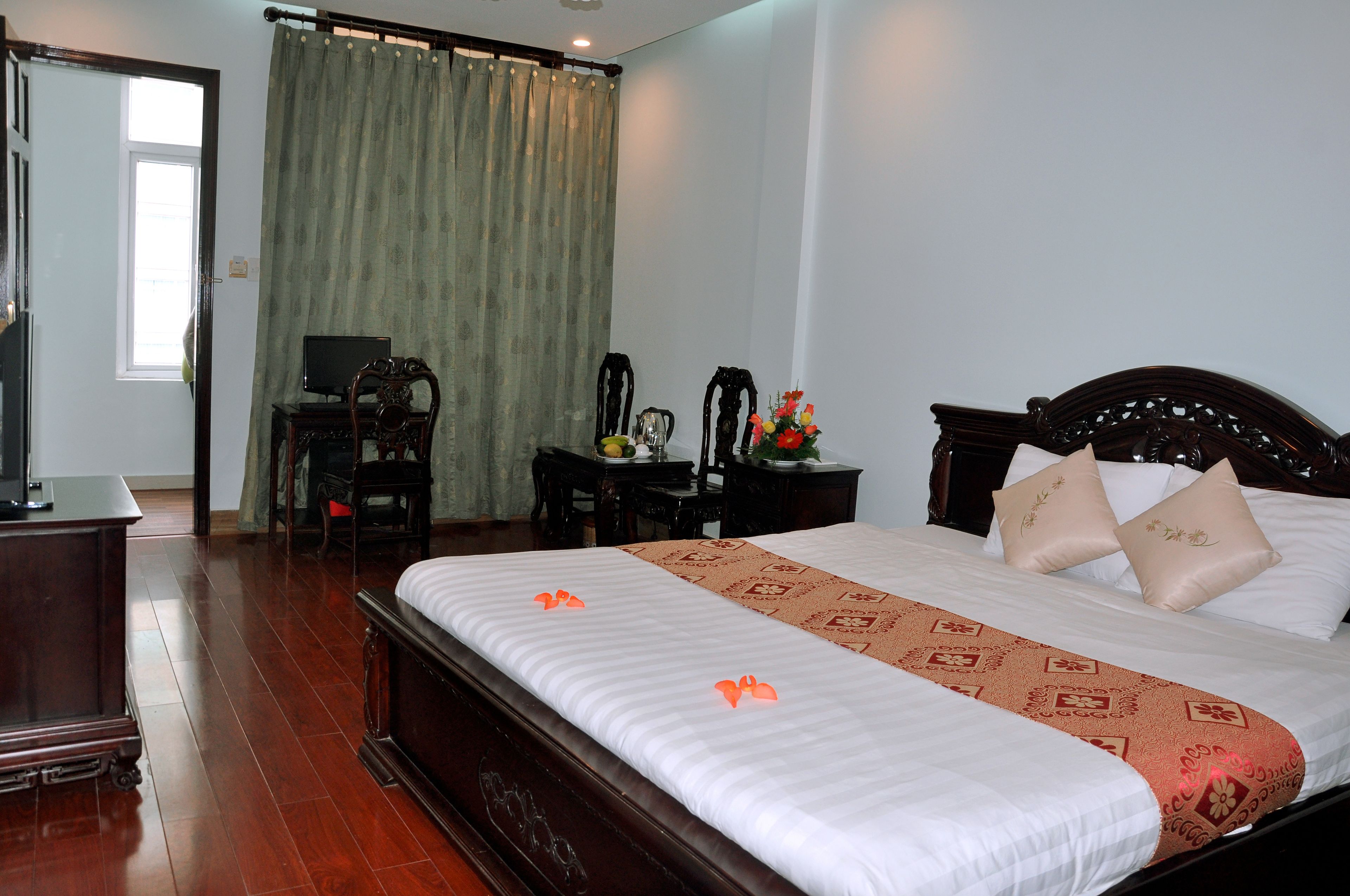 A hotel room with a large bed, a desk with a computer, a chair, and a small table with a vase of flowers.