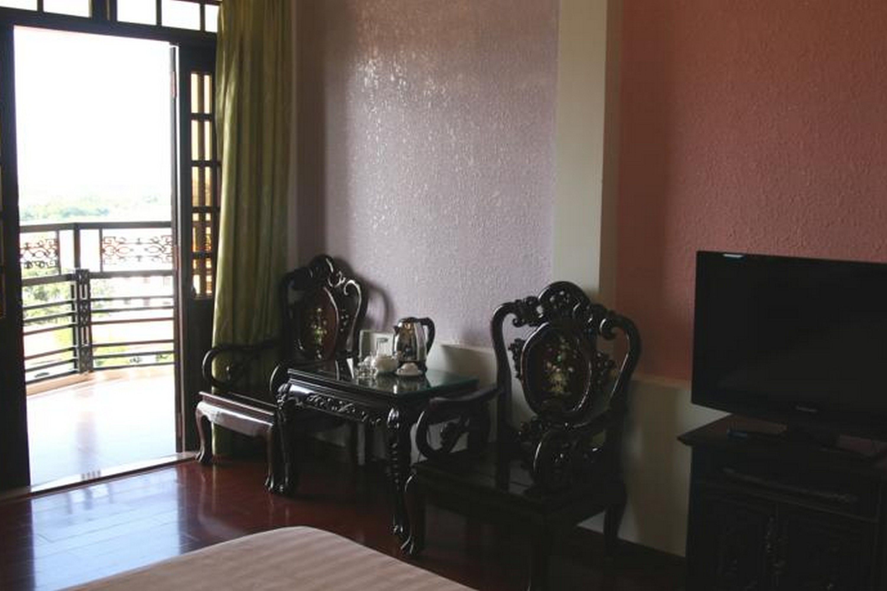 A room with a bed, a TV, a table with chairs, and a view through a window.