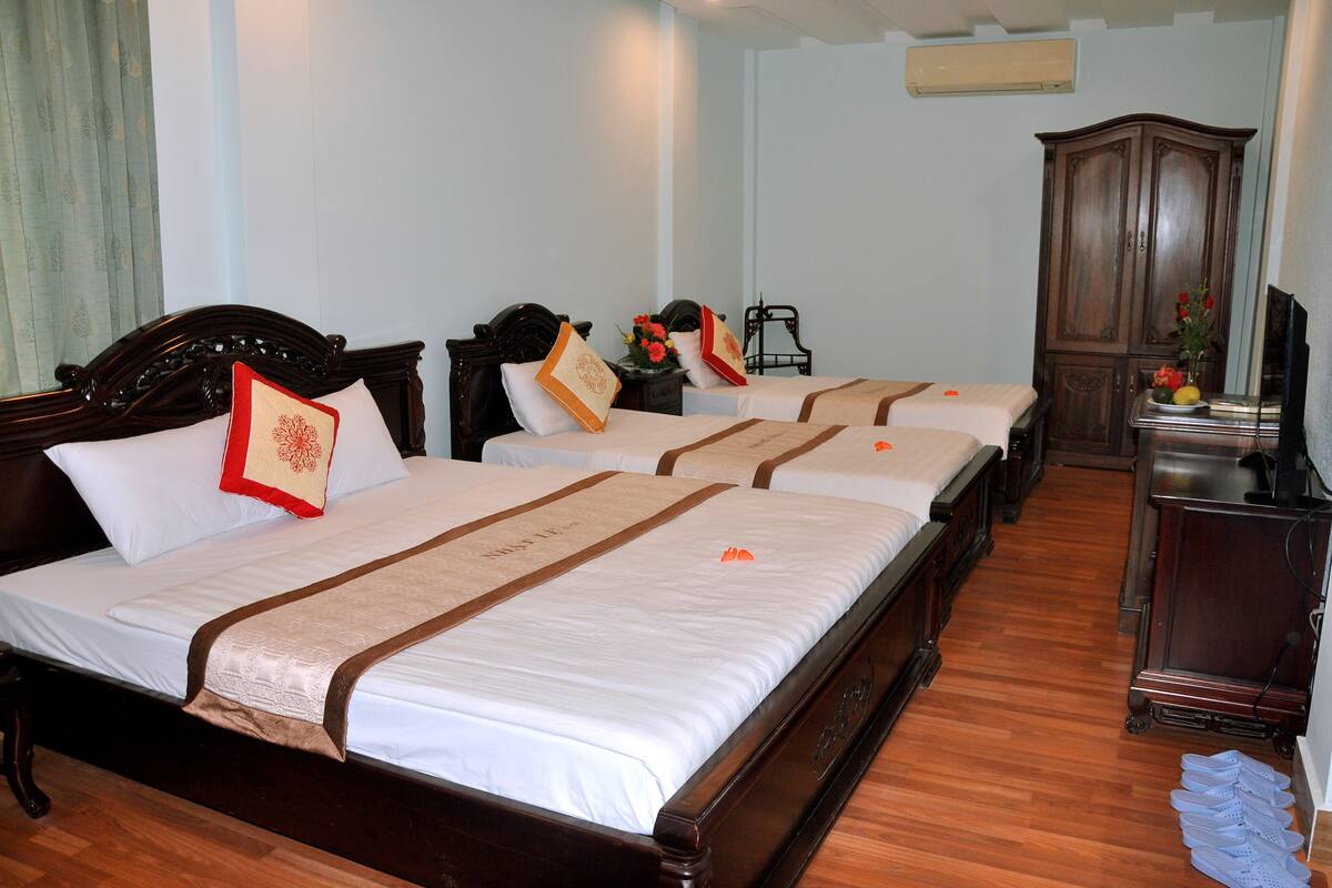 A hotel room with three beds, wooden headboards, and a wardrobe.