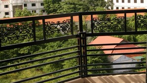 A balcony with a black metal railing and a view of a building with a red roof and greenery in the background. - Thai Binh Hotel 2 (Hue)