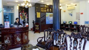 A reception area with a wooden reception desk, ornate chairs, a chandelier, and a large pillar. - Thai Binh Hotel 2 (Hue)
