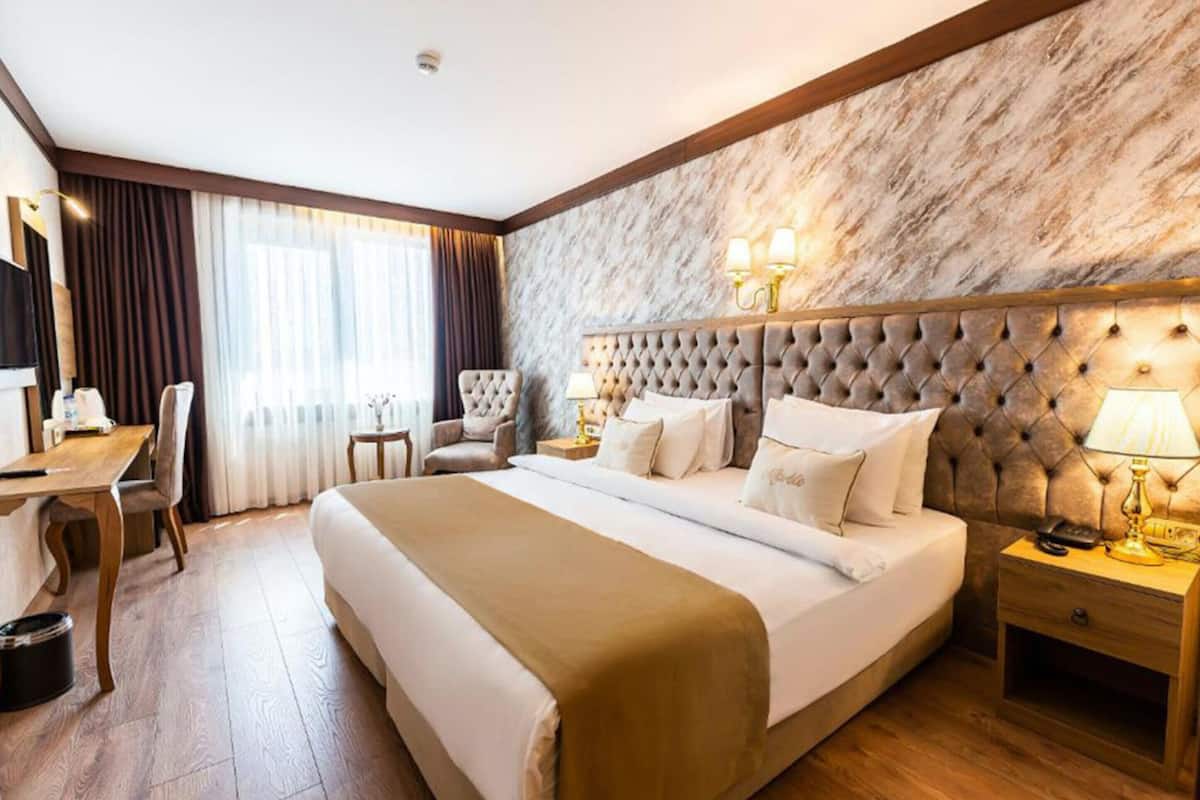 A hotel room with a large bed, a desk, a chair, a nightstand with a lamp, and a marble wall.